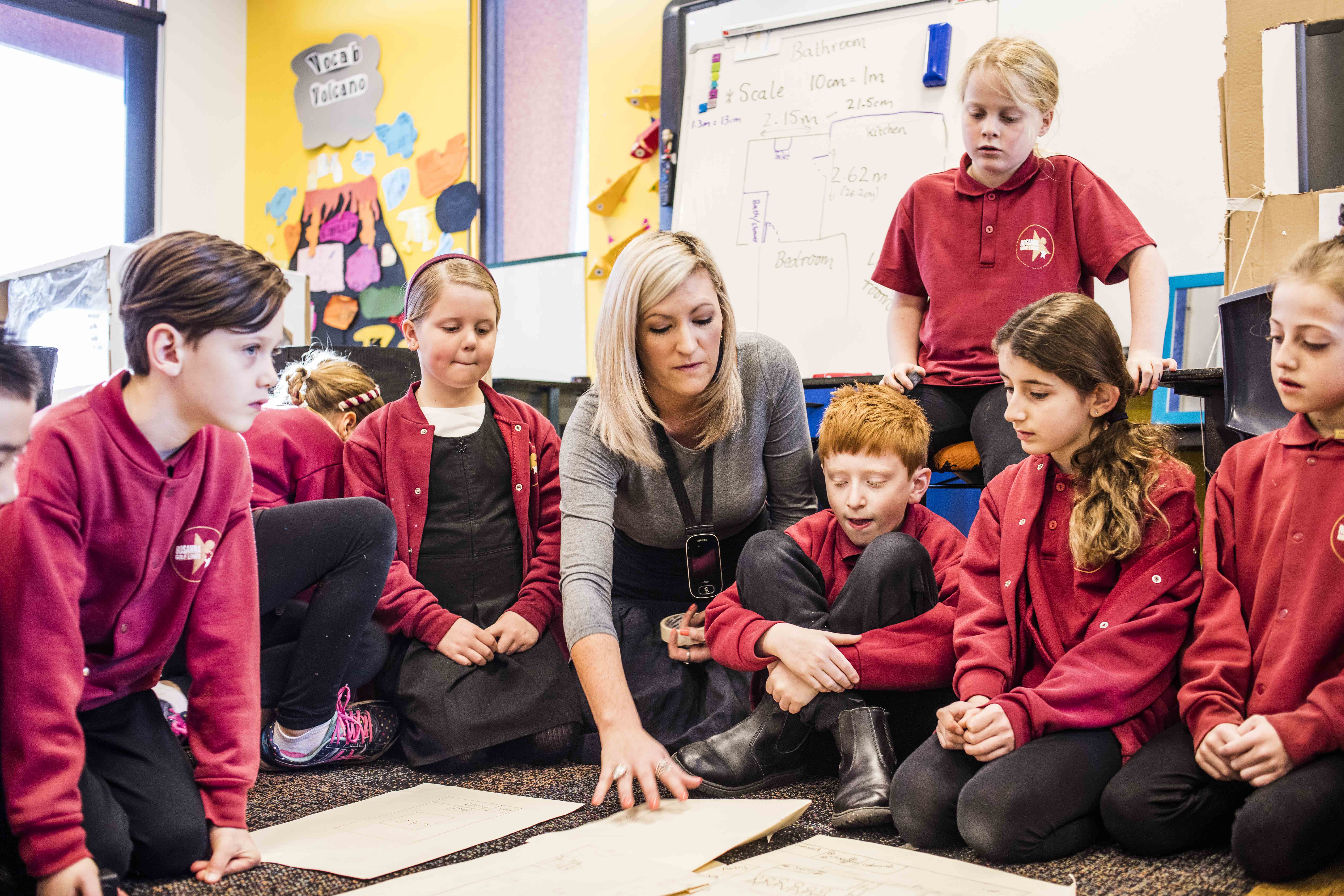 Teacher and students sitting on classroom floor looking at materials on the floor.