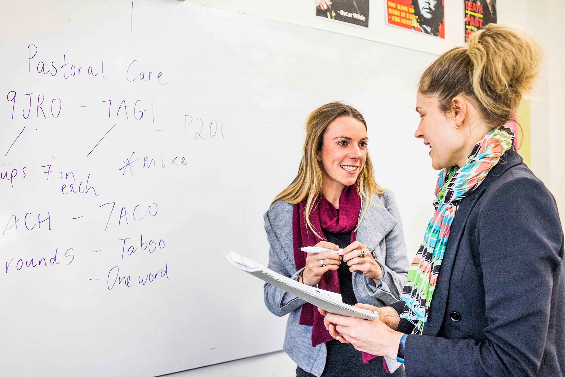Two teachers having a discussion in front of a whiteboard. 
