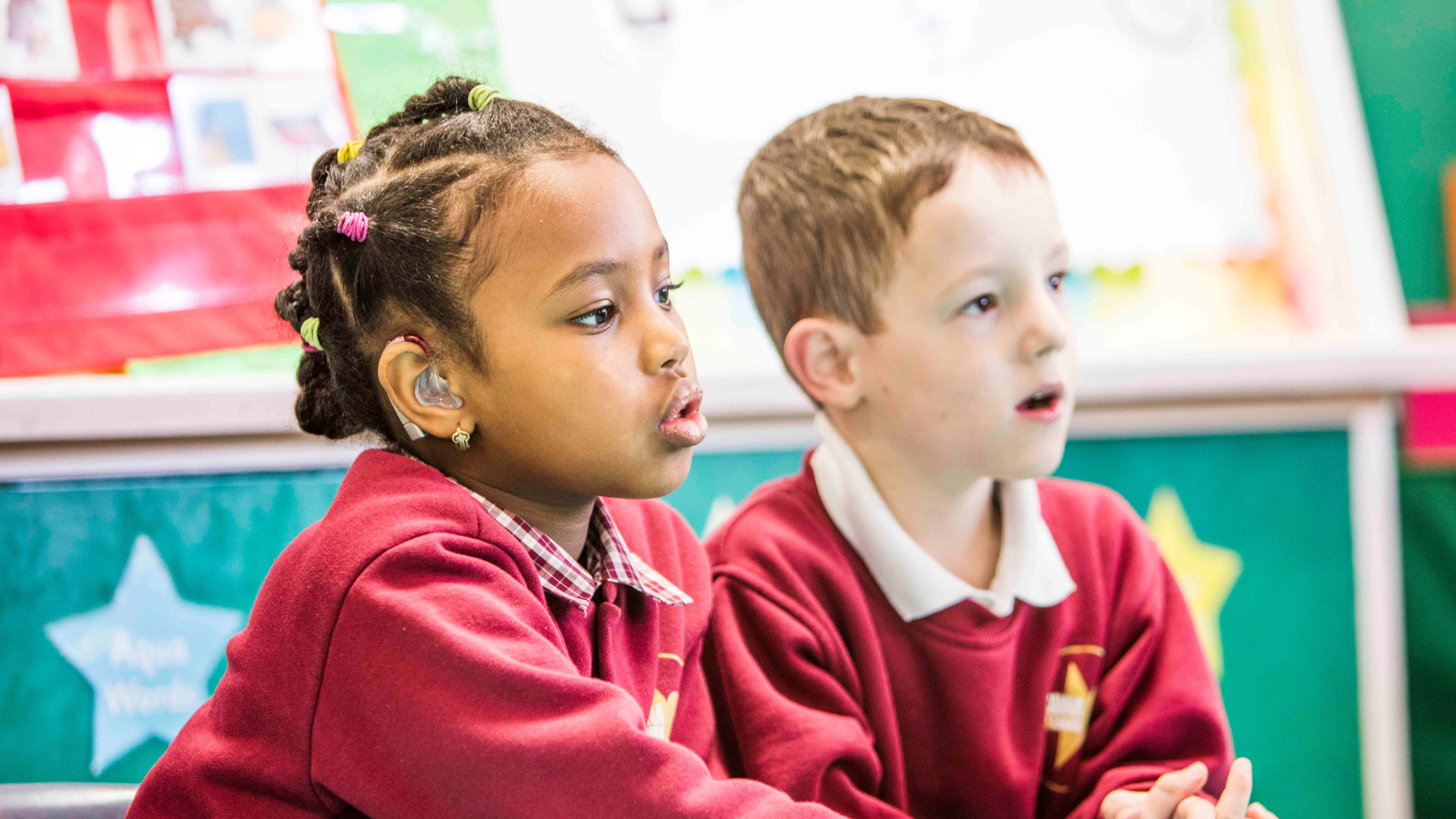 Two students sitting together, one is wearing a hearing aid.