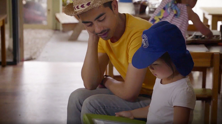 A young learner uses a tablet device with assistance from an educator.