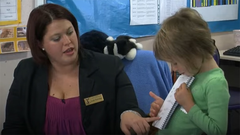 A teacher reading a young learner spelling.